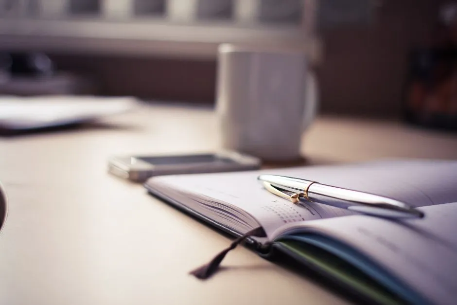 Open desk diary beside a stack of bound newspaper volumes under a reading lamp
