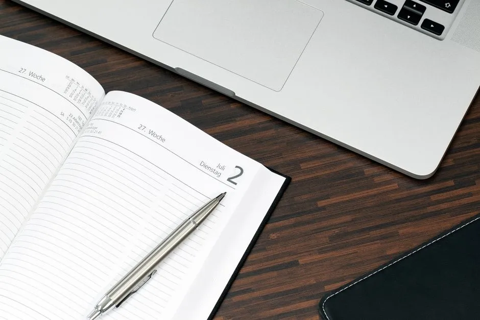 Open desk diary turned to a single date, beside a laptop showing a page of history entries